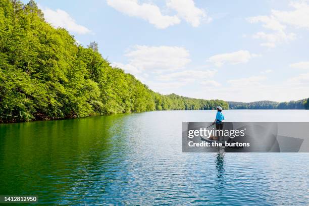 woman stand up paddling on an idyllic lake in summer - paddleboarding ストックフォトと画像