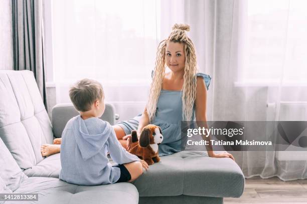 young woman with dreadlocks have a fun with little son at home. cozy interior. - chien en peluche photos et images de collection