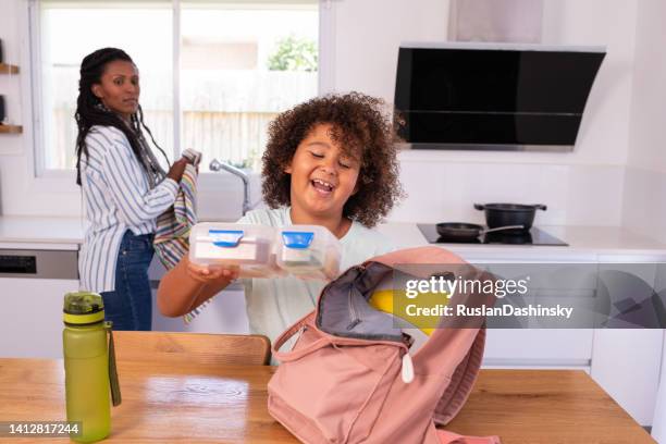 happy elementary-age child putting a lunch box into a pink backpack before going to school. - open rucksack stock pictures, royalty-free photos & images