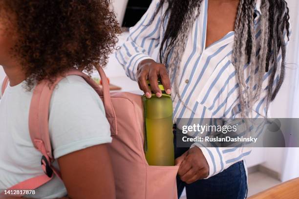 mother putting a water bottle into a pink backpack at home in the kitchen. - packing kids backpack stockfoto's en -beelden