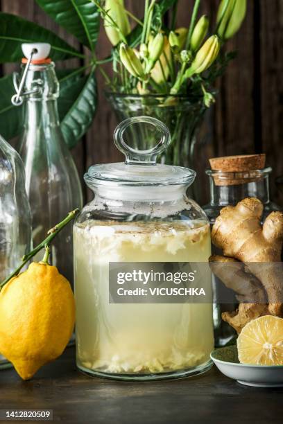 jar with homemade ginger ale at kitchen counter with ginger, lemon, glass bowls and flowers at rustic wooden background - homemade root beer stock pictures, royalty-free photos & images