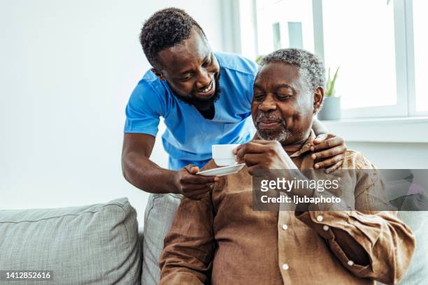 home caregiver helping a senior man drinking a cup of coffee at a nursing home. - african american man helping elderly bildbanksfoton och bilder