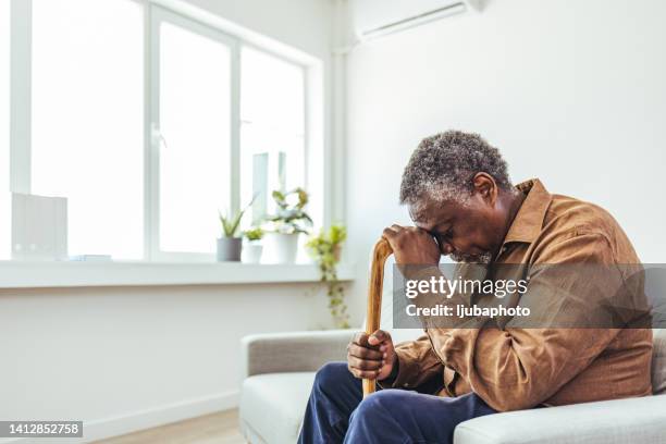 thoughtful elderly man sitting alone at home with his walking cane - walking cane stock pictures, royalty-free photos & images