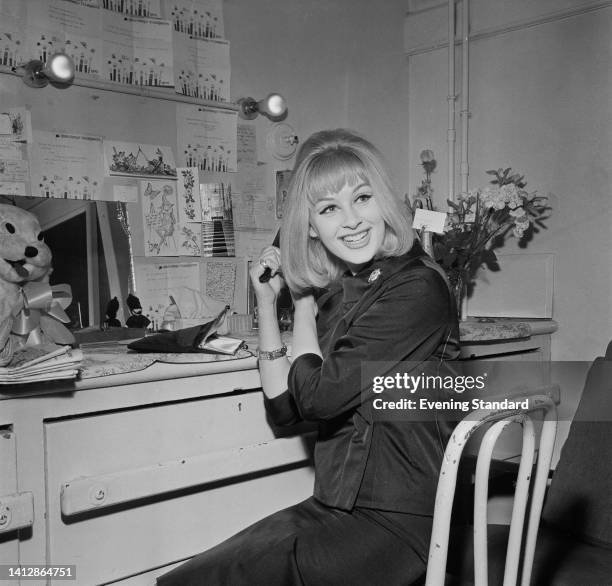 British actress Gabriella Licudi turns in her chair as she brushes her hair while sitting at a dressing table, with drawings and telegrams pinned to...