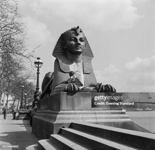 Man reading a newspaper as he sits between the front paws of one of two bronze sphinxes on the Victoria Embankment in Westminster, London, England,...