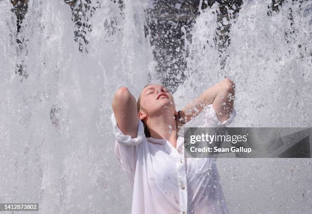 Young woman visiting from Paris, who said she did not mind being photographed, cools off in a fountain at Lustgarten park on August 04, 2022 in...