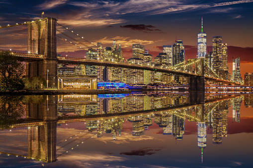 Brooklyn Bridge and New York City Skyline with Manhattan Financial District and World Trade Center, Reflected in East River at Orange Blue Sunset.