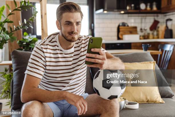 joven con balón de fútbol, usando teléfono inteligente - apuestas deportivas fotografías e imágenes de stock
