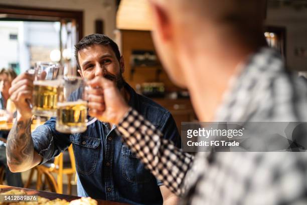 male friends talking and toasting a beer at a bar - friday stock pictures, royalty-free photos & images