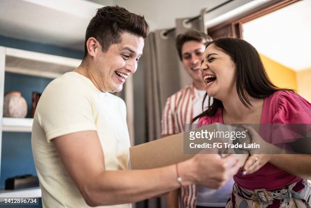 young man receiving gift from friends at home - house warming stock pictures, royalty-free photos & images
