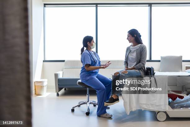 female doctor gestures while talking to female patient in er - doctors stock pictures, royalty-free photos & images