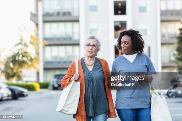 senior woman with caregiver walking, carry reusable bags - chores stock pictures, royalty-free photos & images