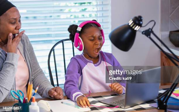 la abuela ayuda a la niña con la tarea en la computadora portátil, bostezando - desk lamp fotografías e imágenes de stock