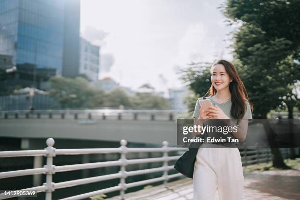 asiatische chinesin, die morgens mit dem smartphone am flussufer entlang geht - chinese woman outside walking stock-fotos und bilder