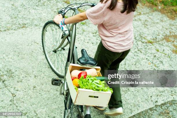 unrecognizable woman carrying a bicycle loaded with the purchase of organic vegetables - shopping with bike stock-fotos und bilder