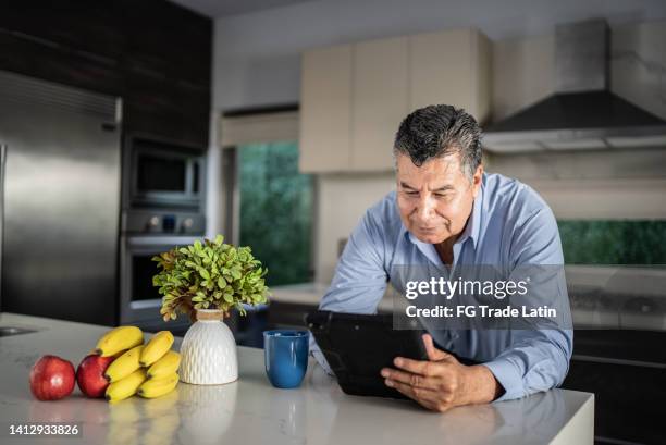 mature man using digital tablet in the kitchen at home - baby boomer home stock pictures, royalty-free photos & images