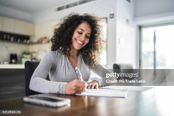 mid adult woman filling document at home - signing paperwork stock pictures, royalty-free photos & images