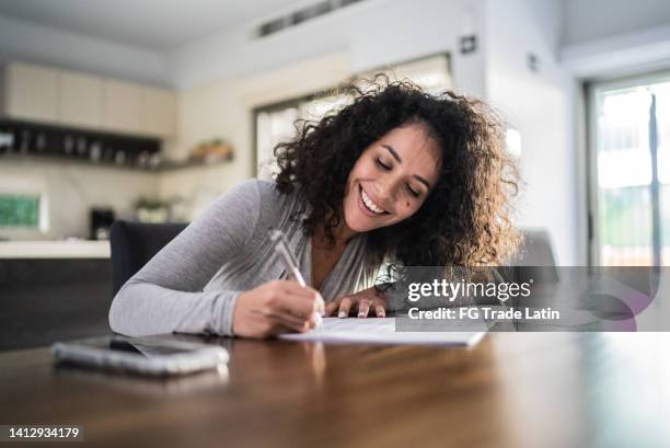 mid adult woman filling document at home - achievement certificate stock pictures, royalty-free photos & images