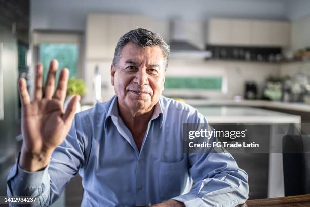 senior man doing a video call at home - camera point of view - hand waving stock pictures, royalty-free photos & images