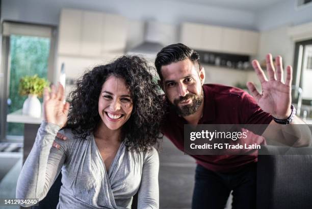 mid adult couple doing a video call at home - camera point of view - waving imagens e fotografias de stock