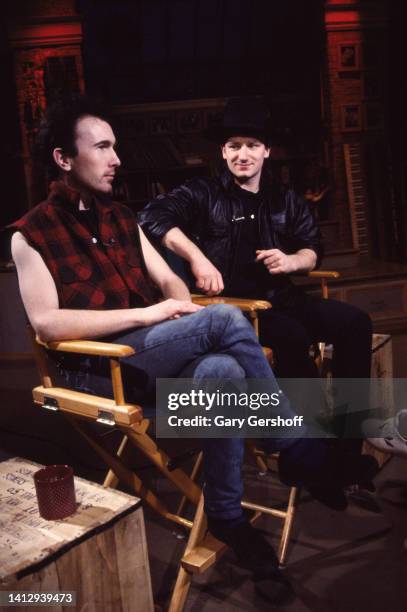 View of Rock musicians the Edge and Bono , both of the group U2, as they sit in director's chairs during an interview on MTV at Teletronic Studios,...