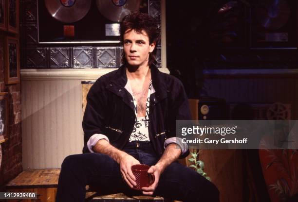 View of Australian-American Pop musician and actor Rick Springfield as he sits on a crate, a coffee mug in his hands, during an interview on MTV at...