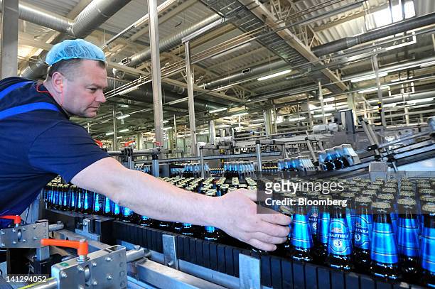 An employee inspects bottles of Baltika-branded lager as they move along a conveyor belt at the Carlsberg A/S production plant in Kiev, Ukraine, on...