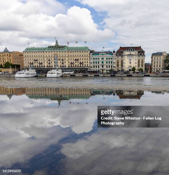 hotels in stockholm's downtown harbor reflected in large puddle with dramatic blue sky and clouds above - grand hotel stockholm stock-fotos und bilder