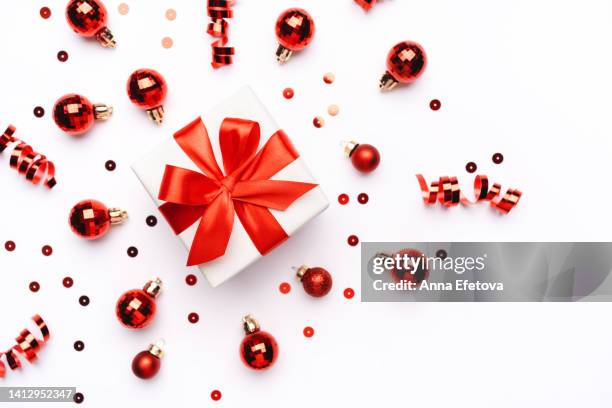 white gift box with red silk ribbon bow on white background with many red confetti, christmas tree balls and ribbons. new year celebration concept. photography from above - red tinsel stock pictures, royalty-free photos & images