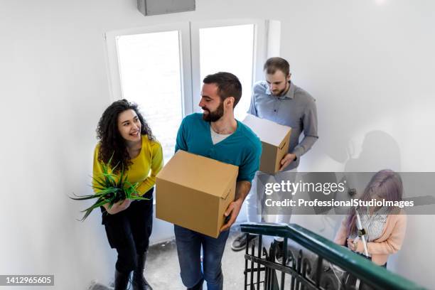 a smiling four friends are carrying paper boxes upstairs into a new home on moving day. - student visa stockfoto's en -beelden