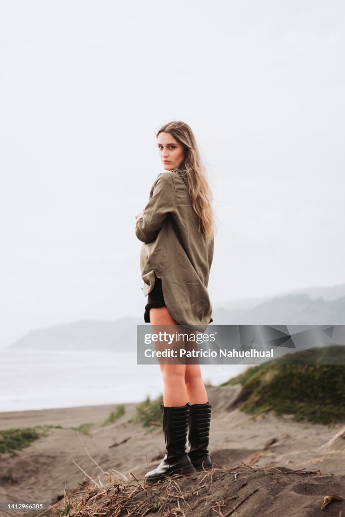 Young female blonde model standing on the beach with the sea behind