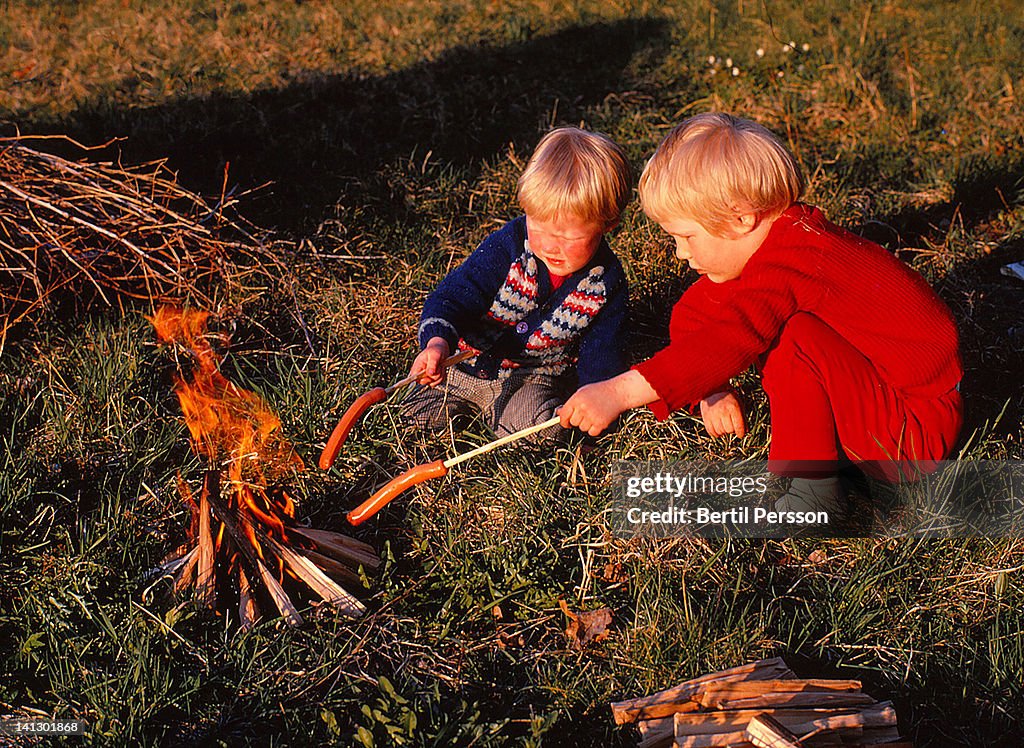 Sisters barbecuing sausages by open fire