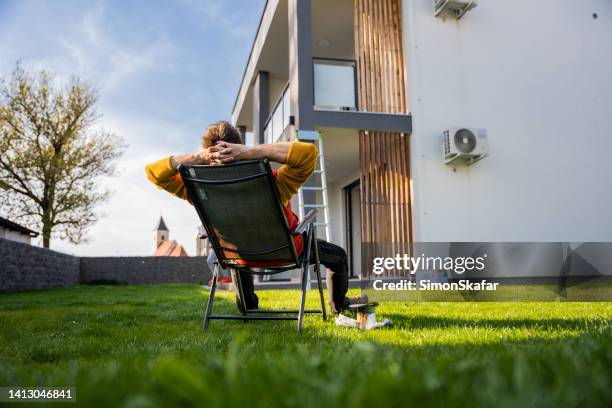 homme fatigué se relaxant sur une chaise confortable par l’équipement dans la cour à l’extérieur de l’appartement - homme transat jardin photos et images de collection