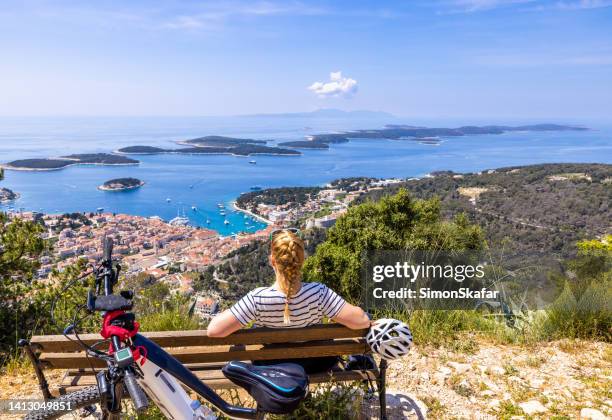 woman sitting on bench and enjoying view of town from top of mountain - hvar croatia stock pictures, royalty-free photos & images