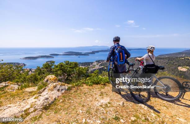 male and female biker with bicycles enjoying view of town from top of mountain - hvar stockfoto's en -beelden