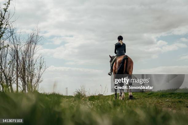 rückansicht der frau, die auf einem grasbewachsenen feld gegen bewölkten himmel reitet - equestrian eventing stock-fotos und bilder