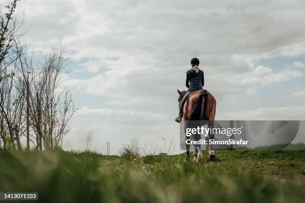rear view of woman riding horse on grassy field against cloudy sky - hästfälttävlan bildbanksfoton och bilder