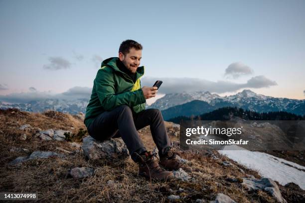 glücklicher männlicher wanderer mit handy, während er auf dem gipfel des berges sitzt - mann auf berg mit smartphone stock-fotos und bilder