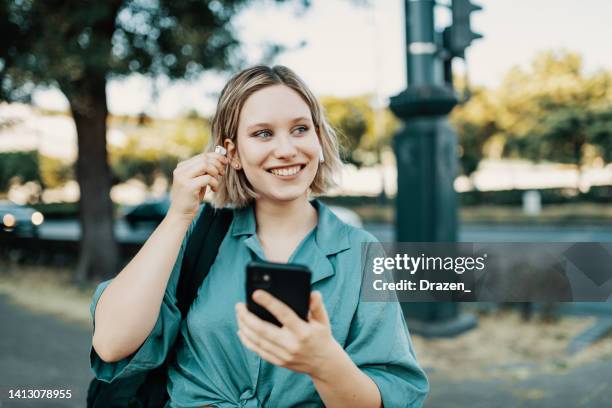 jeune femme utilisant un téléphone intelligent à l’extérieur et écoutant de la musique sur des écouteurs - in ear headphones photos et images de collection