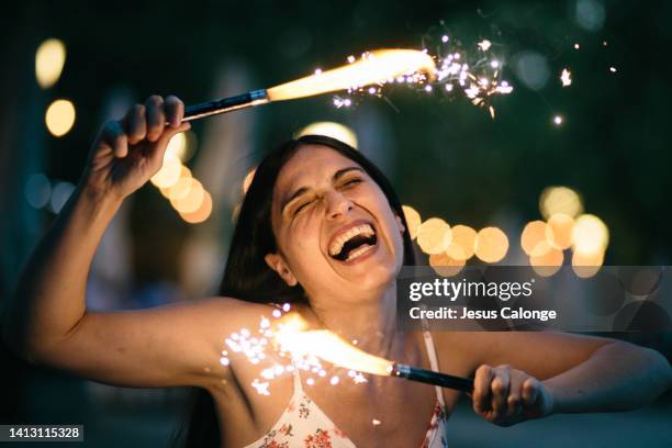 woman with two sparkler (pyrotechnics). laughing and with an expression of celebration and happiness. happiness, celebration, party concept - smiling jesus - fotografias e filmes do acervo