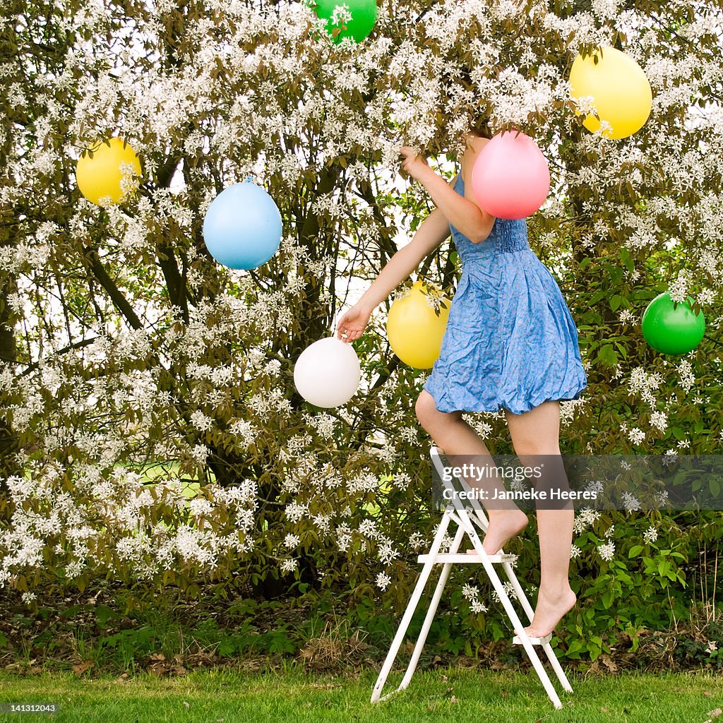Girl hanging balloons in tree