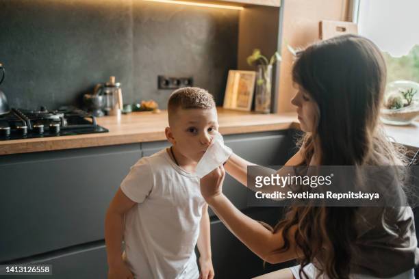 mother wipes her son's face with a napkin after a family dinner - childhood hunger stock pictures, royalty-free photos & images
