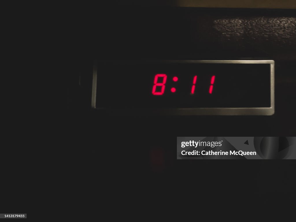 Retro digital alarm clock in dark room in front of stack of books in the shadows