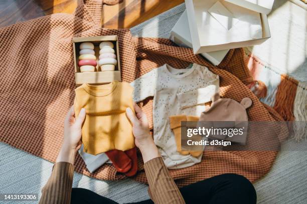 high angle shot of pregnant woman unpacking delivered parcels of baby clothings and accessories from shopping online, laying on the floor against sunlight. mother-to-be. preparation for a new family member. expecting a new life concept - baby clothes stock pictures, royalty-free photos & images