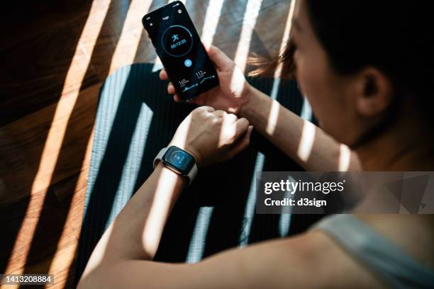 young active asian woman exercising at home, using smartphone health and fitness apps to monitor and track training performance and activity. recording health status with mobile phone. health and fitness training with technology. healthy living lifestyle - smartwatch imagens e fotografias de stock