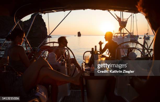 group of friends on a sailboat, enjoying a glass of wine at sunset - aperitief stockfoto's en -beelden