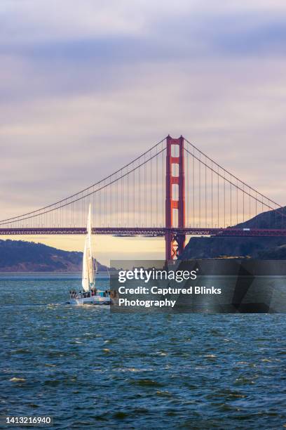 a yacht sailing near golden gate bridge during sunset from the sea - bucht-von-san-francisco stock-fotos und bilder