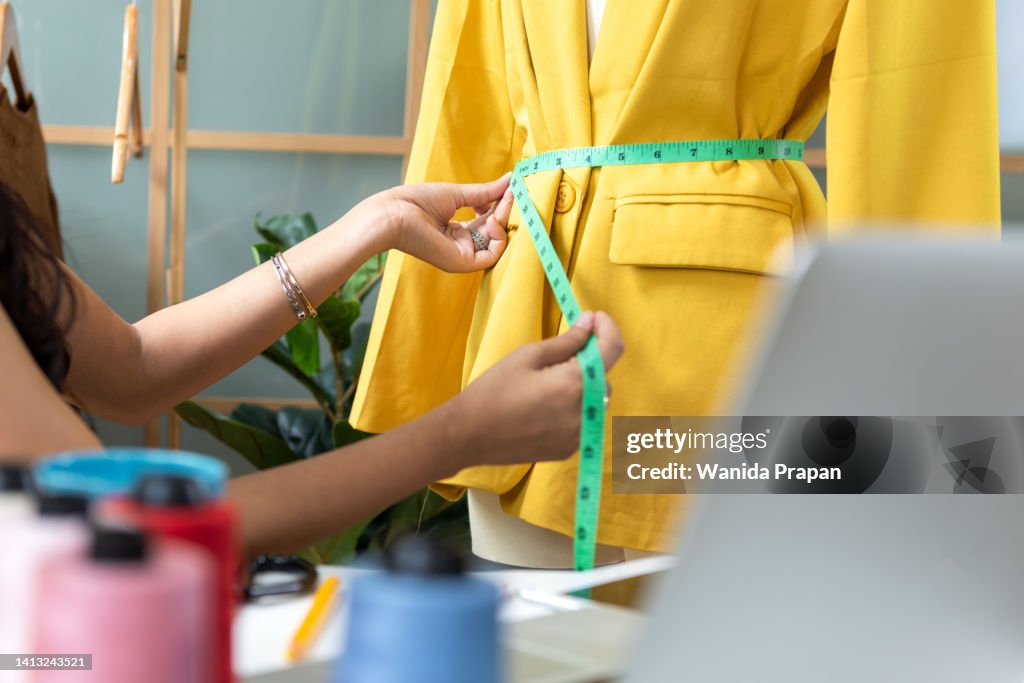 Close up hands designer work designer fashion in the showroom. Mannequins stylish tailor measurements and cloth rail background. Business small Concept