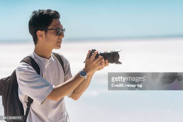 young male tourist taking videos and photos with his camera on white salt in salt lake - holding sunglasses stockfoto's en -beelden