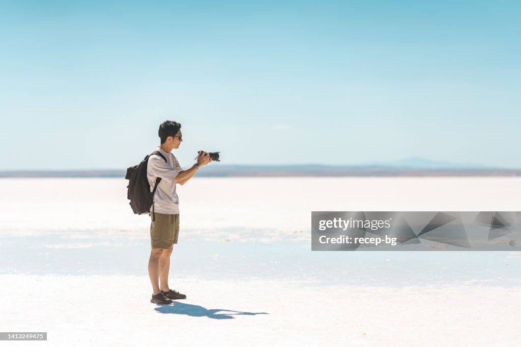 Young male tourist taking videos and photos with his camera on white salt in Salt Lake